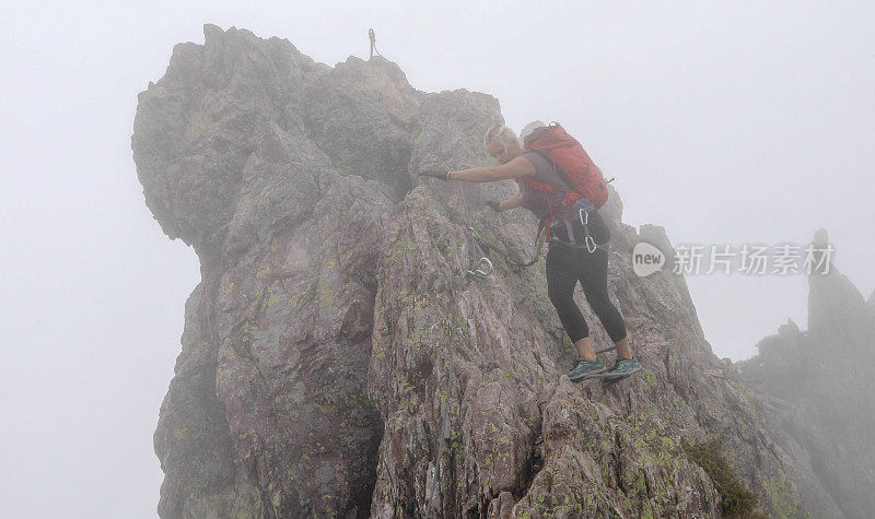 一个成熟的女人在雾中沿着岩石脊上的via ferrata移动